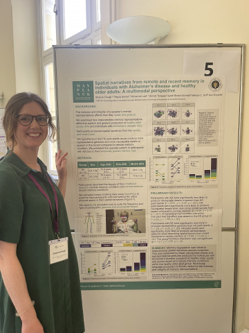 Sharice Clough stands beside a research poster titled "Spatial narratives from remote and recent memory in individuals with Alzheimer’s disease and healthy older adults: A multimodal perspective." She is smiling, wearing glasses, and a green dress with a conference badge.