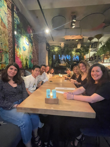 A group of people sitting at a long wooden table in a stylish restaurant with modern art and greenery.