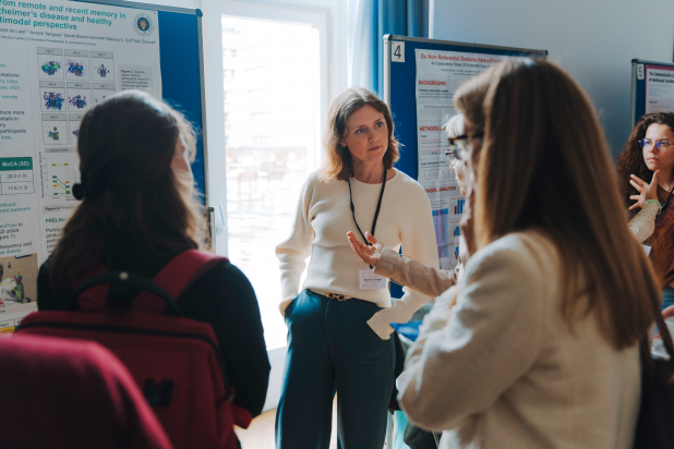 A woman in a white cardigan discusses her poster on gestures and multimodal communication with a group at a conference.